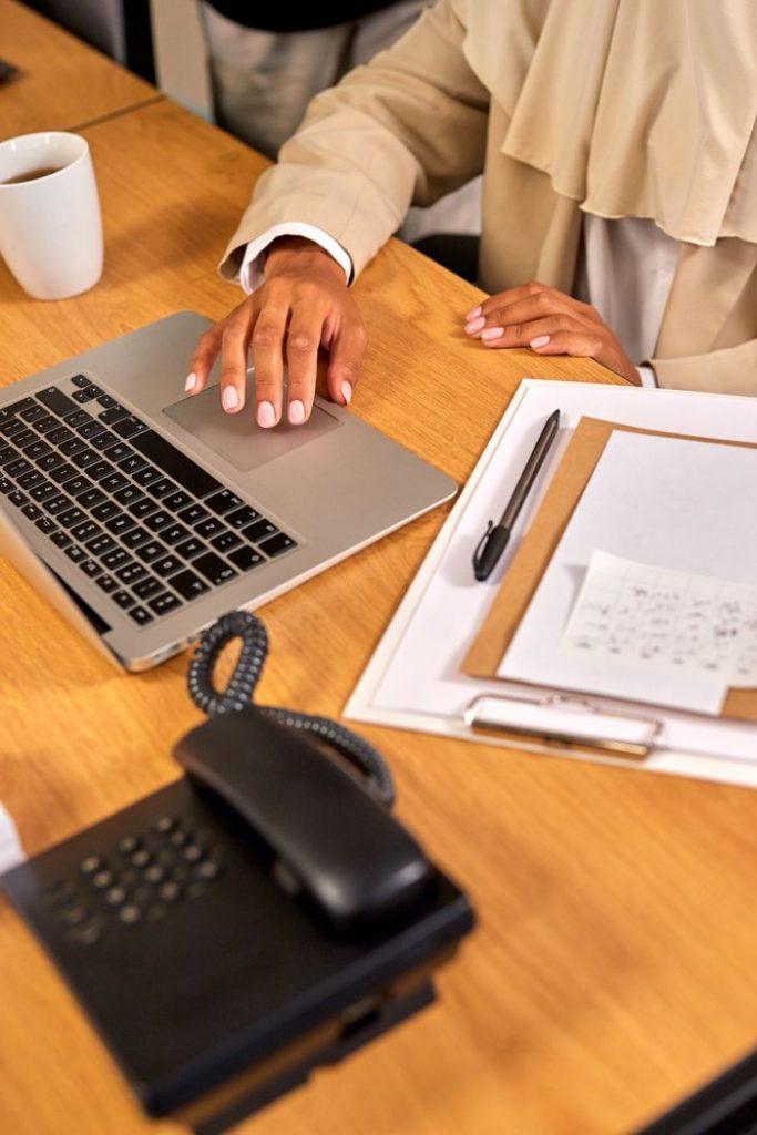 Professional woman working on a laptop at an organized desk with coffee, clipboard, and phone.