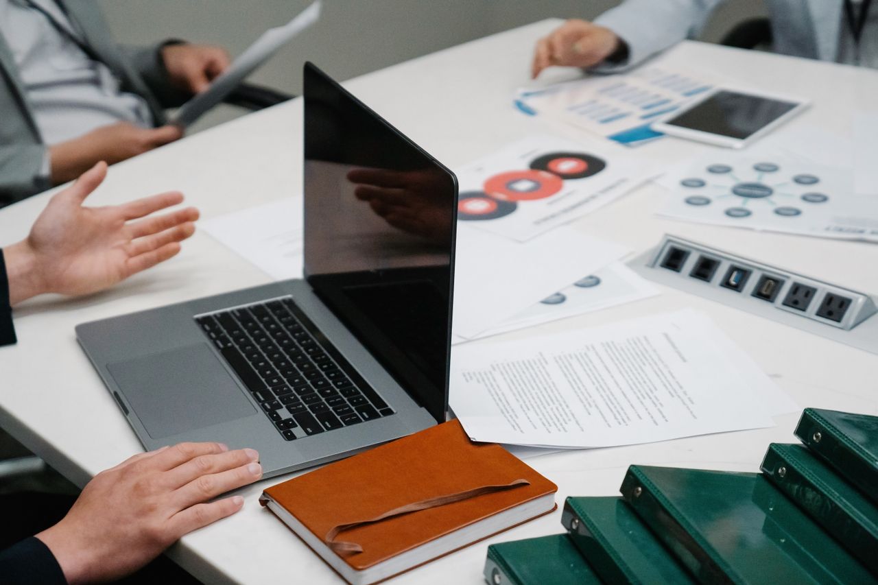 why-choose-us Close-up of a business meeting table with a laptop, documents, and discussion underway.